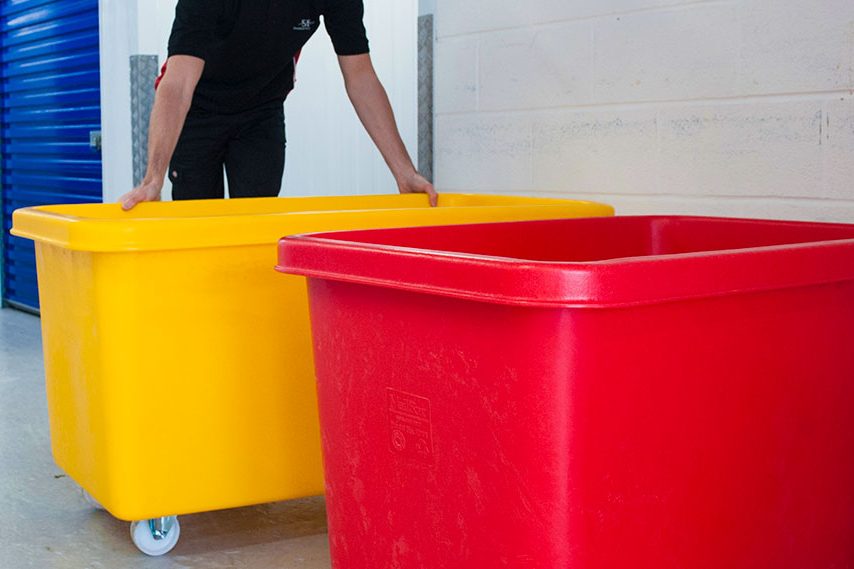 Kunststoffrollwagen Person schiebt gelbe und rote Aufbewahrungsbehälter in einem Lagerraum.